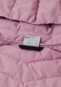 Interno di una giacca imbottita rosa con cuciture a zigzag, caratterizzato da un'etichetta di stoffa con la scritta "Io ero qui:" e un accento elastico nero.