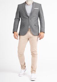 Blazer grigio con una trama testurizzata, chiusura a un bottone, revers a punta, abbinato a pantaloni beige a gamba tapered e sneaker bianche. Sotto una semplice maglietta.