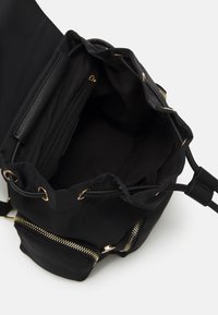 Sac à cordon noir en tissu avec des accents de fermeture éclair et des accessoires dorés. Intérieur spacieux avec une poche zippée. Texture lisse.