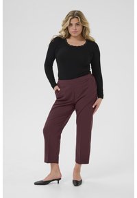 Haut noir à manches longues avec encolure en dentelle, associé à un pantalon bordeaux cintré avec poches latérales et une texture lisse, porté avec des mules noires.