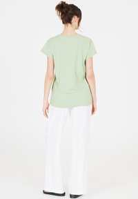 Ljust grön t-shirt med kort ärm och rund hals, matchad med vita vida byxor och svarta platta skor. Slät tygtextur.