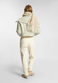 Ljusgrön kort jacka i strukturerad tyg med ribbad krage, tillsammans med en beige scarf med fransar, krämfärgade skräddarsydda byxor och beige klackskor.