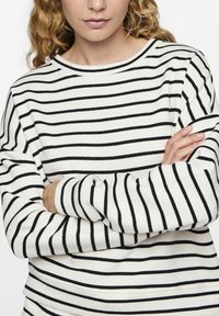 Pull blanc avec des rayures noires horizontales, col rond et manches longues. La texture du tissu semble douce et lisse.