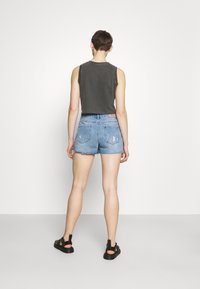 Top sin mangas gris con dobladillo sin rematar, combinado con pantalones cortos de mezclilla claros y desgastados de cintura alta y sandalias negras. Texturas suaves y ajuste casual.