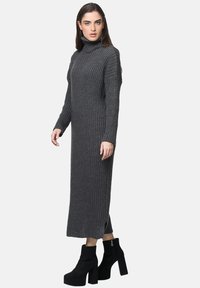 Graues geripptes Strick-Turtleneck-Kleid mit langen Ärmeln, seitlichen Schlitzen und knöchelhohen schwarzen Plateaustiefeln. Glatte Textur, figurbetonter Schnitt.