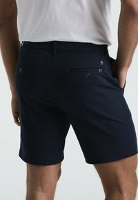 Marineblaue Shorts aus einem glatten Stoff, mit zwei Gesäßtaschen mit Knopfverschluss und einem kleinen Logodetail am Bund.