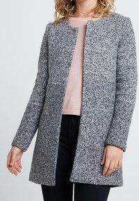 Szary płaszcz wełniany z okrągłym dekoltem i bez zapięcia, o długich rękawach i prostym kroju, noszony na jasnoróżowym swetrze.