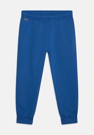 Pantalons de survêtement en coton bleu avec taille élastique, poignets effilés et détail logo brodé. Texture lisse et design décontracté.