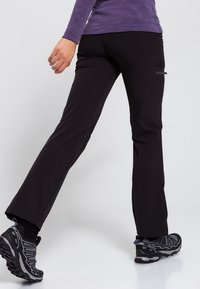 Svart utomhusbyxor med rak bendesign, tillverkade av lätt material, med en zipficka och en slät yta.