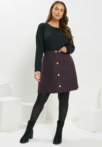 Musta pitkähihaine paita yhdistettynä purppura leopardikuvioiseen hameeseen, jossa on kultaiset napit ja levenevä muoto. Mustat sukkahousut ja nilkkurit.