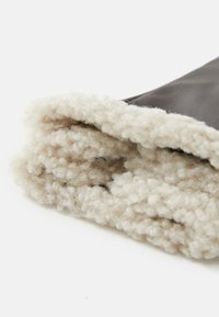 Mănușă din piele maro cu un manșon moale din blană bej, texturat pentru căldură. Marginile sunt coase cu grijă, evidențiind contrastul de material.