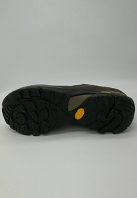 Suola in gomma nera con battistrada profondo per una buona aderenza, con una parte superiore marrone e beige. Logo del marchio Vibram in giallo.