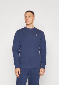Donkerblauwe sweatshirt van zacht materiaal, met lange mouwen, geribde manchetten en een klein logo-detail op de borst.
