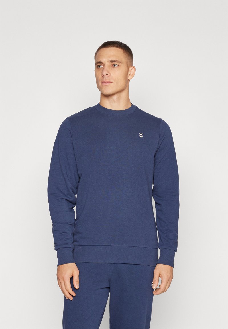 Donkerblauwe sweatshirt van zacht materiaal, met lange mouwen, geribde manchetten en een klein logo-detail op de borst.
