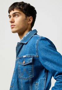 Jeansjacka i en medelblå nyans med en klassisk design, som har bröstfickor, sömnadsdetaljer och en varumärkesetikett på kragen.