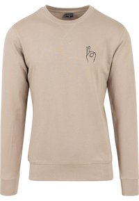Sweater bej din bumbac, cu guler rotund și mâneci lungi. Pe pieptul stâng se află o imprimare simplă a unui gest cu mâna, de culoare neagră.
