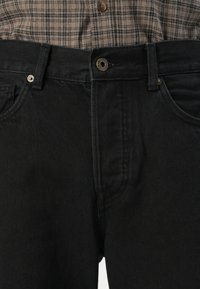 Jeans de denim negro con una textura suave, diseño de cinco bolsillos y herrajes dorados contrastantes en el botón. Presenta un corte recto.