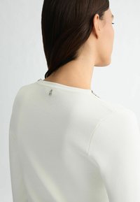 Top bianco in maglia con scollatura rotonda, adornato da un sottile dettaglio sul retro e dotato di una texture liscia.