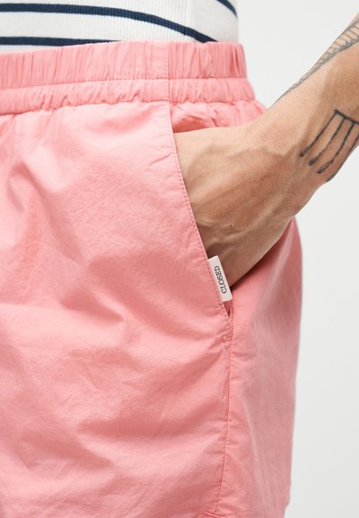 Ροζ σορτς με ελαστική μέση, πλαϊνή τσέπη και μικρή ετικέτα με την ένδειξη "CLOSED". Λείο, ελαφρύ ύφασμα με ματ φινίρισμα.