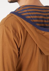 Sudadera de algodón marrón con un forro interior a rayas en azul y marrón, con una textura suave y un cuello acanalado en contraste.