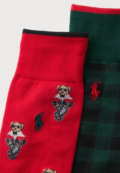 Deux paires de chaussettes, une rouge avec des motifs d'ours en peluche et de joueur de polo, l'autre à carreaux verts et noirs avec un logo joueur de polo rouge.