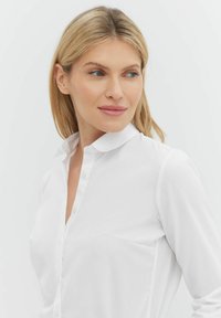 Biała koszula zapinana na guziki z kołnierzykiem, wykonana z gładkiego materiału. Posiada kieszeń na piersi oraz subtelne detale szwów, a także długie rękawy.