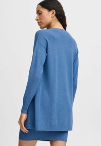 Blauwe gebreide jurk met lange mouwen, een ronde hals en geribbelde zoomdetails. Soepele textuur, knielengte met een relaxte pasvorm.