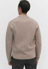 Beige trui met lange mouwen, een zachte textuur en een relaxed fit, met een ronde zoom en subtiele stikdetails op de schouders.