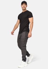 Camiseta negra de manga corta combinada con pantalones cargo grises que cuentan con múltiples bolsillos y puños elásticos, completada con zapatillas deportivas blancas.