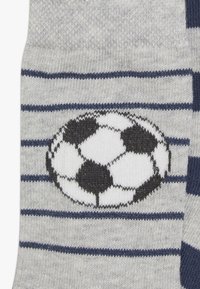 Sosete gri cu dungi bleu marin. Prezintă un grafic central cu o minge de fotbal alb-negru. Fabricate dintr-un material moale, texturat.