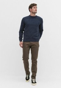 Mörkblå stickad tröja med rund halsringning, parat med ljusbruna byxor och svarta sneakers med vita snören. Jämn textur och avslappnad passform.