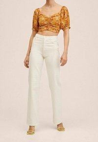 Haut court à manches courtes à imprimé floral en jaune et orange, associé à un jean blanc taille haute à jambes larges et des sandales jaunes à lanières.