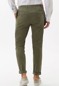 Wąskie spodnie chino w kolorze oliwkowej zieleni, wykonane z bawełny, o zwężanym kroju, z podwiniętymi nogawkami, dwie tylne kieszenie zapinane na guziki, zestawione z jasnymi trampkami.
