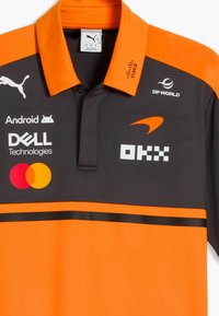 Polo deportivo en naranja y negro con los logotipos de los patrocinadores Puma, Android, Dell Technologies, Mastercard, Cisco, DP World y OKX.
