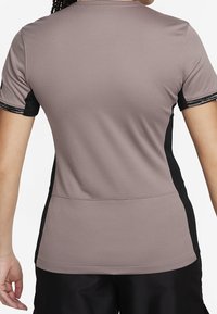 Camiseta atlética de manga corta en un suave color malva con tejido texturizado. Detalles en negro en los lados y las mangas. Diseño sencillo y funcional.