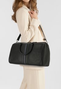 Schwarze Tasche aus synthetischem Leder mit zwei Henkeln, einem abnehmbaren Riemen und drei vertikalen Streifen in Marineblau und Grün. Glatte Textur, geräumiges Design.