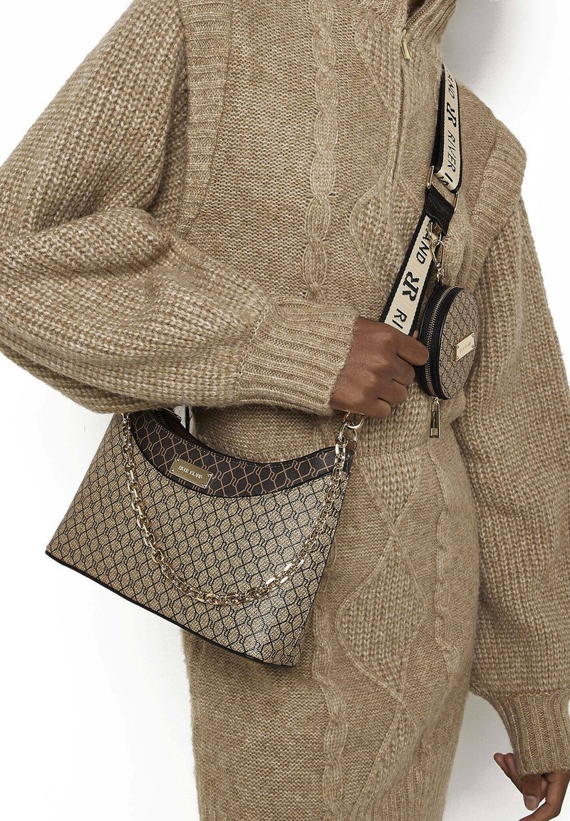 Hnědá kabelka s vzorem a řetězovým detailem, s hladkým povrchem a kulatou peněženkou připevněnou řemínkem vedle pleteného oděvu.