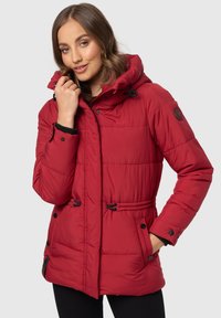 Červená izolačná puff jacket s kapucňou, vybavená čiernymi kovovými prvkami, šnúrkami a kontrastnými čiernymi manžetami. Šitie vytvára prešívanú textúru.