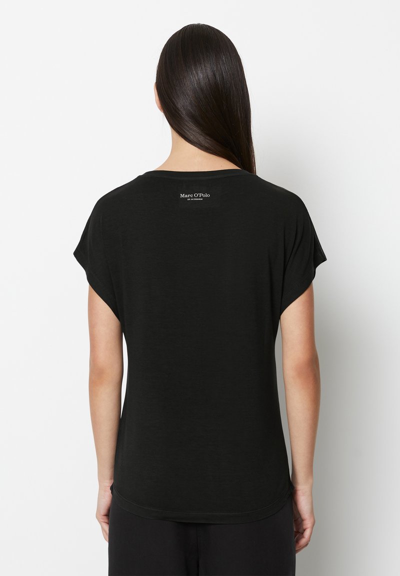 Schwarzes T-Shirt mit rundem Halsausschnitt und kurz gerollten Ärmeln. Mit einem kleinen Logo auf der oberen Rückseite in einer kontrastierenden Farbe.