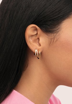 Gold- und Silbercreolen mit einer glatten goldenen Oberfläche und einem Band, das mit kleinen klaren Edelsteinen verziert ist. Am Ohr einer Person getragen.