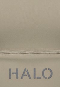 Beżowa koszulka sportowa o gładkiej fakturze, z widocznym zapięciem na zamek i logo "HALO" w ciemnoszarym kolorze.