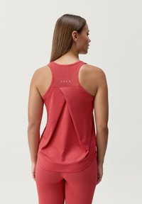 Czerwona sportowa koszulka na ramiączkach z okrągłym dekoltem, z siateczkowymi wstawkami oraz luźnym krojem, w zestawie ze stającymi legginsami. Gładka faktura na całej powierzchni.
