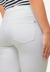 Jeans con vita elastica bianca dal design aderente, dotati di due tasche posteriori, cuciture sottili e una finitura liscia e non strutturata.