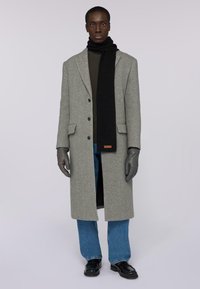 Šedý vlněný kabát s černým šátkem, zeleným žebrovaným svetrem, modrými džínami a černými rukavicemi. Obsahuje precizní střih a zapínání na knoflíky.