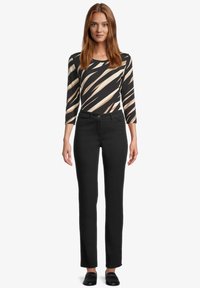 Czarne dopasowane dżinsy w połączeniu z czarnym i beżowym prążkowanym topem z długim rękawem. Top ma okrągły dekolt i rękawy sięgające do łokcia.