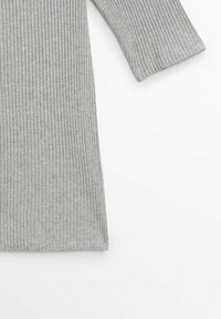 Tissu tricoté côtelé gris à manches longues montrant une partie d'une manche et le corps d'un vêtement sur fond blanc.