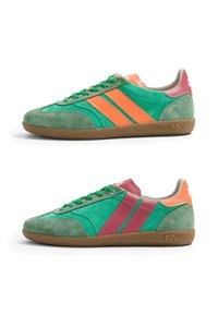 Deux baskets en daim vert avec semelles en gomme, l'une avec des rayures orange et talon, l'autre avec des rayures rose foncé et talon, toutes deux avec des lacets verts.