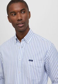 Camicia a righe blu e bianche con bottoni, realizzata in cotone. Presenta una tasca con un piccolo etichetta di marca. Con colletto e dettagli con bottoni.