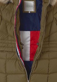 Groene pufferjack met quiltontwerp, voorzien van een ritssluiting en een marineblauwe, rode en witte binnenvoering met een zichtbaar merklabel.