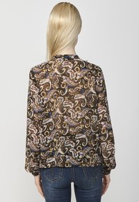 Blusa marrone a fantasia con maniche lunghe, decorata con motivi paisley in rosa, blu e oro. Materiale leggero; dettagli con polsini e scollatura arricciati.